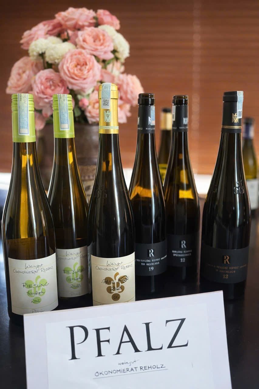 Bottles of Ökonomierat Rebholz wine with pink roses behind a Pfalz region card