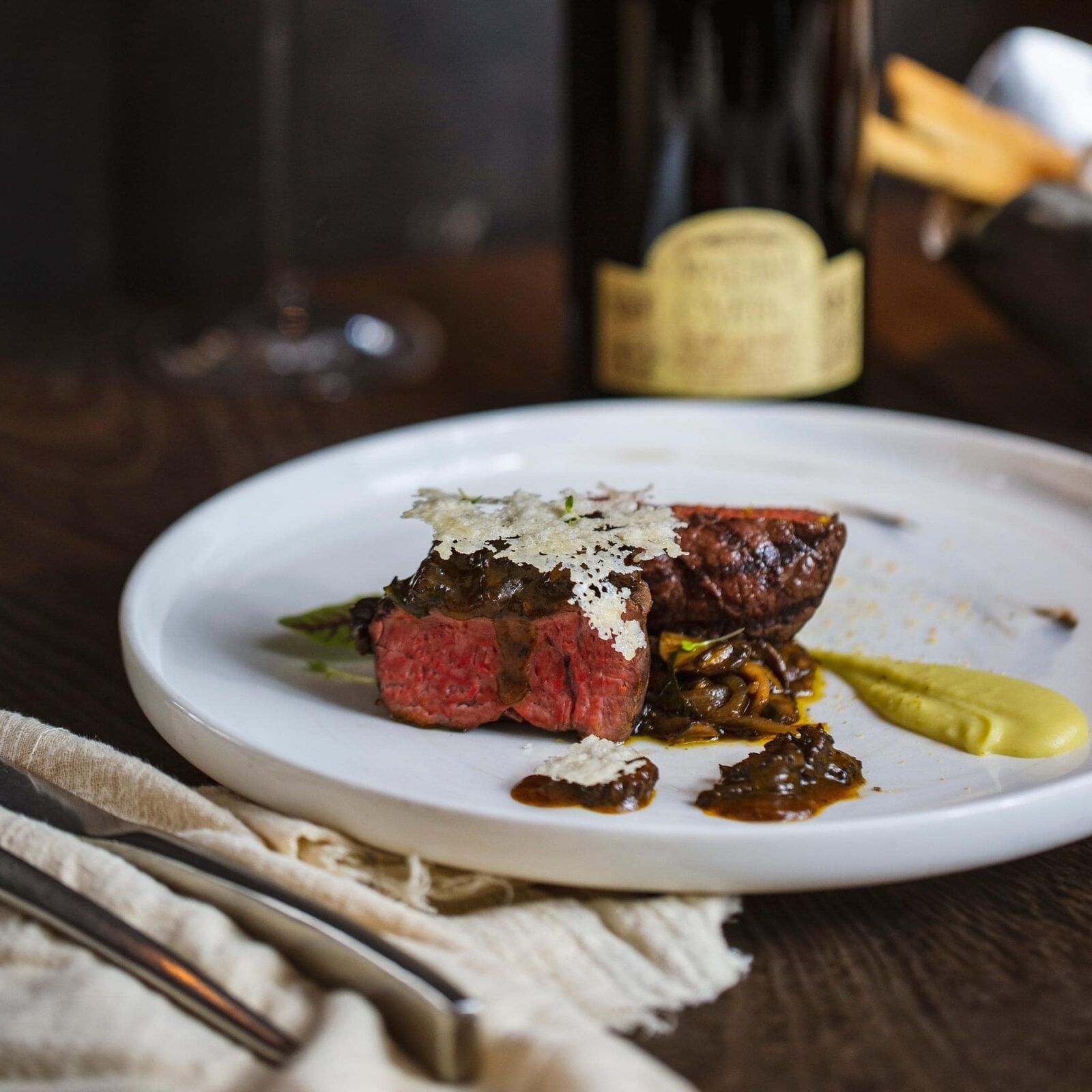 Sliced medium-rare beef fillet with a Parmesan crisp, mushrooms and a yellow purée, a wine bottle in the background