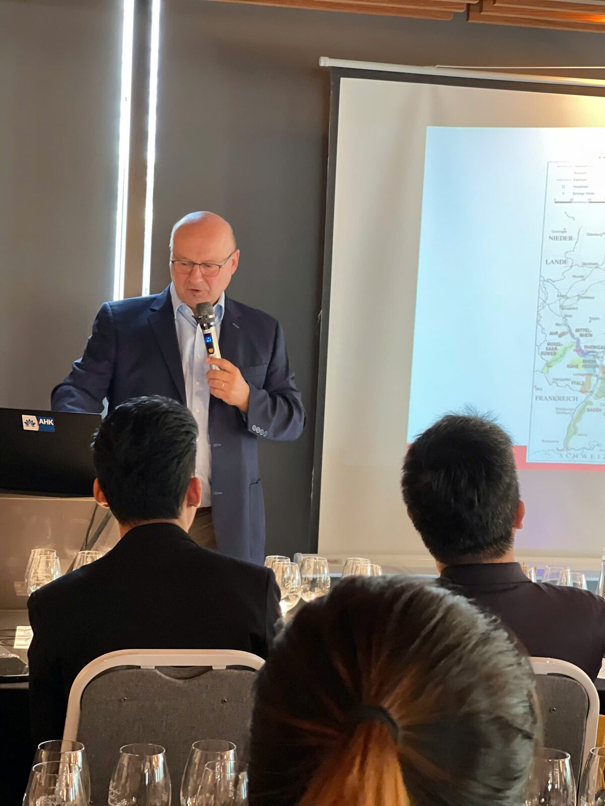 Johannes Selbach speaking into a microphone in front of a projected map of German wine regions